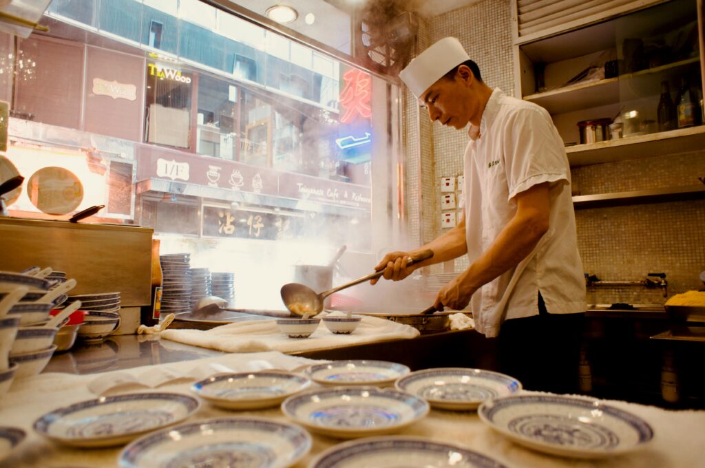 Asian chef in white attire cooking in a bustling Hong Kong restaurant kitchen with steam rising.